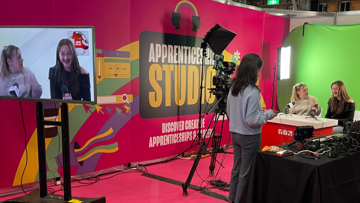 Two students sat in a mock radio student on the BBC stand at UCAS Create Your Future 2023