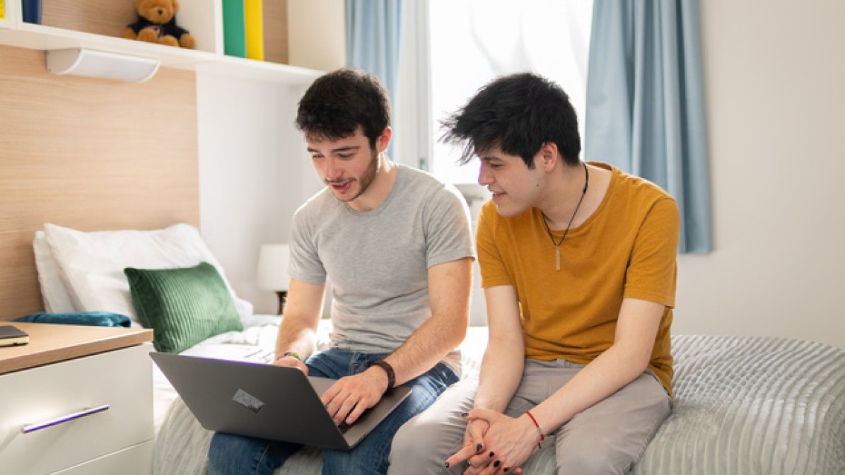 Two students in halls bedroom looking at laptop
